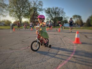Young girl riding bike at the Safe Routes to School Family Fun Night Event in Neenah, Wisconsin in May 2018; orange cone in the background