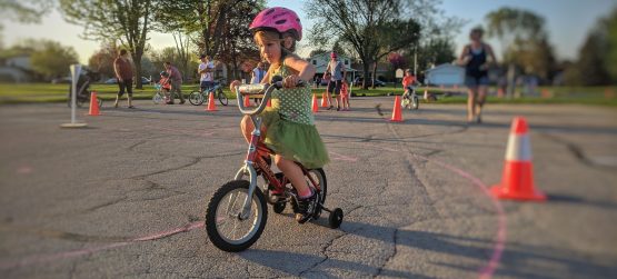 Young girl riding bike at the Safe Routes to School Family Fun Night Event in Neenah, Wisconsin in May 2018; orange cone in the background